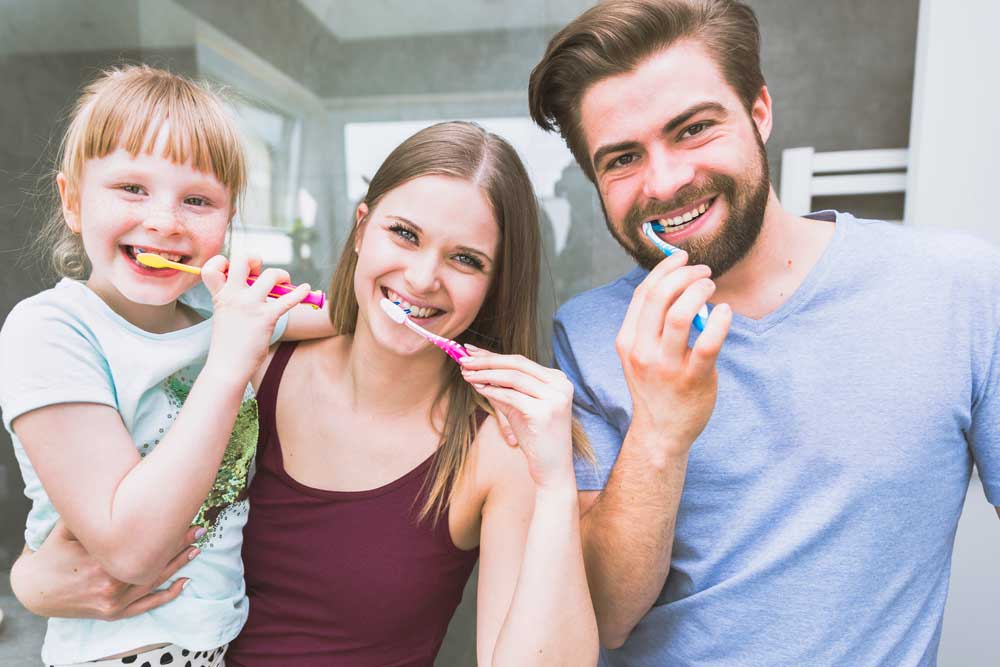 A family of three people brushing their teeth.