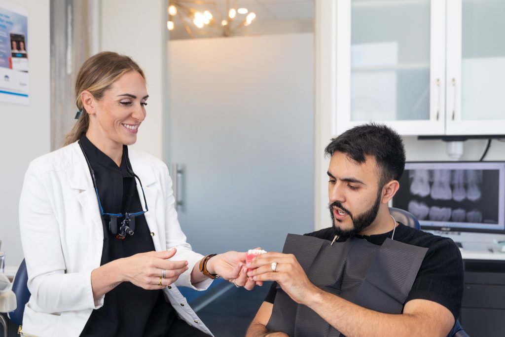 A dentists showing a patient a set of teeth. Learn more about us.