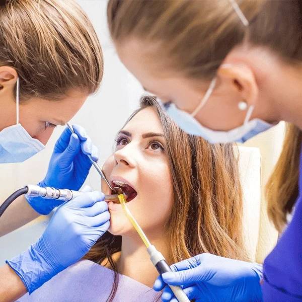Dental professional examines patient's teeth in clinical chair setting with tools and proper protective equipment