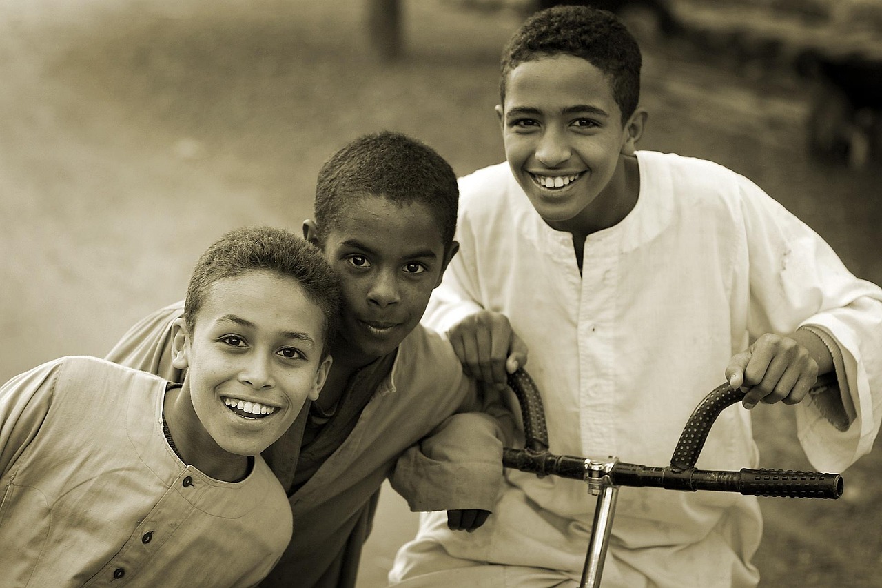 Three boys smiling together outdoors with a bicycle, sepia toned